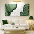 A large rectangular abstract wall art piece with flowing green and white marbled patterns hangs above a white sofa in a modern living room. The room includes a white coffee table, a green pillow, a green lamp, and a vase on a light rug.