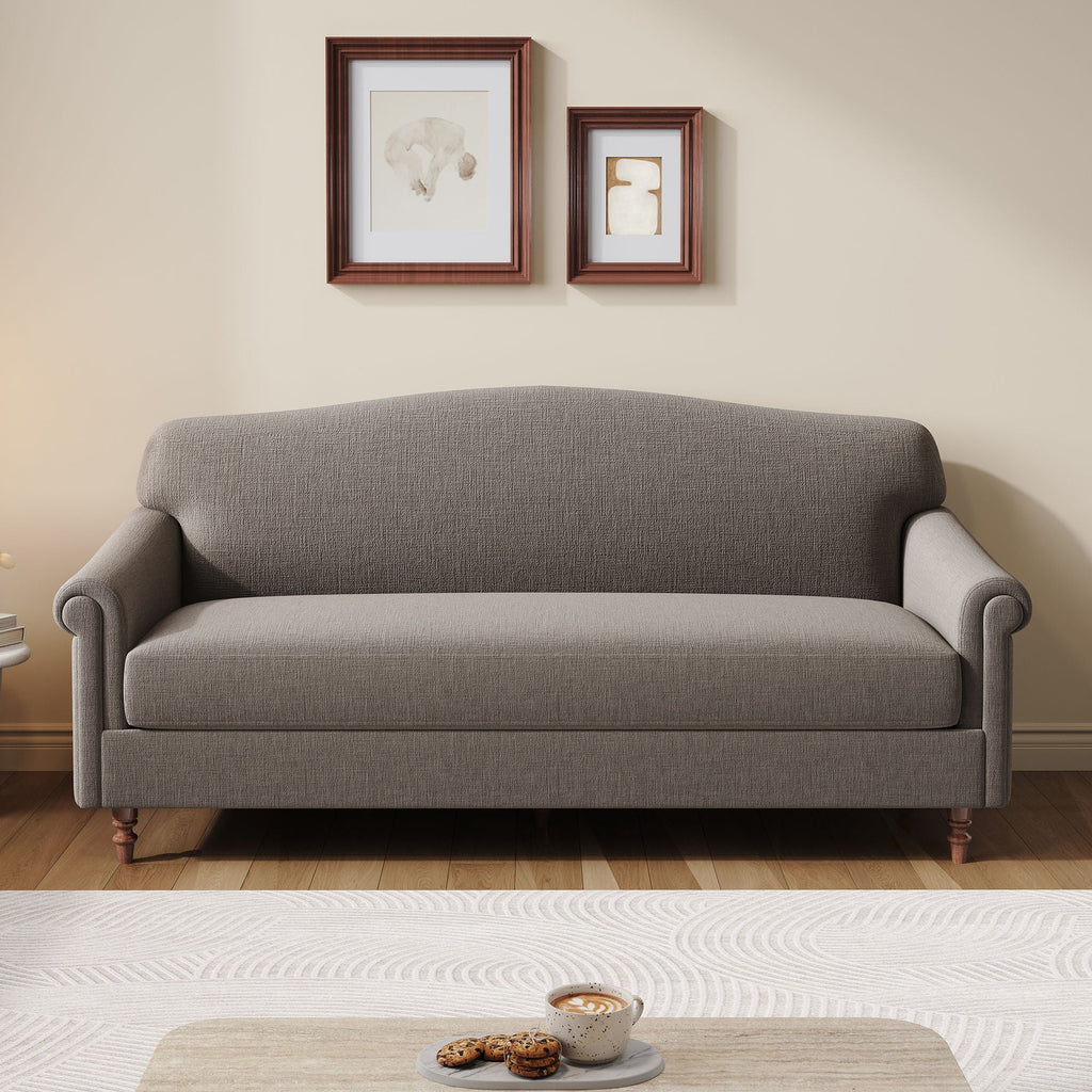 A gray upholstered loveseat sofa with rolled arms and turned wooden legs, shown in a staged living room setting with two framed artworks on the wall above and a small table in the foreground.