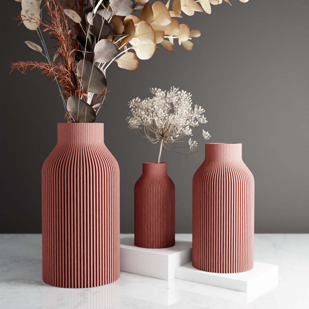 Three ribbed pink vases with dried plants on a gray background