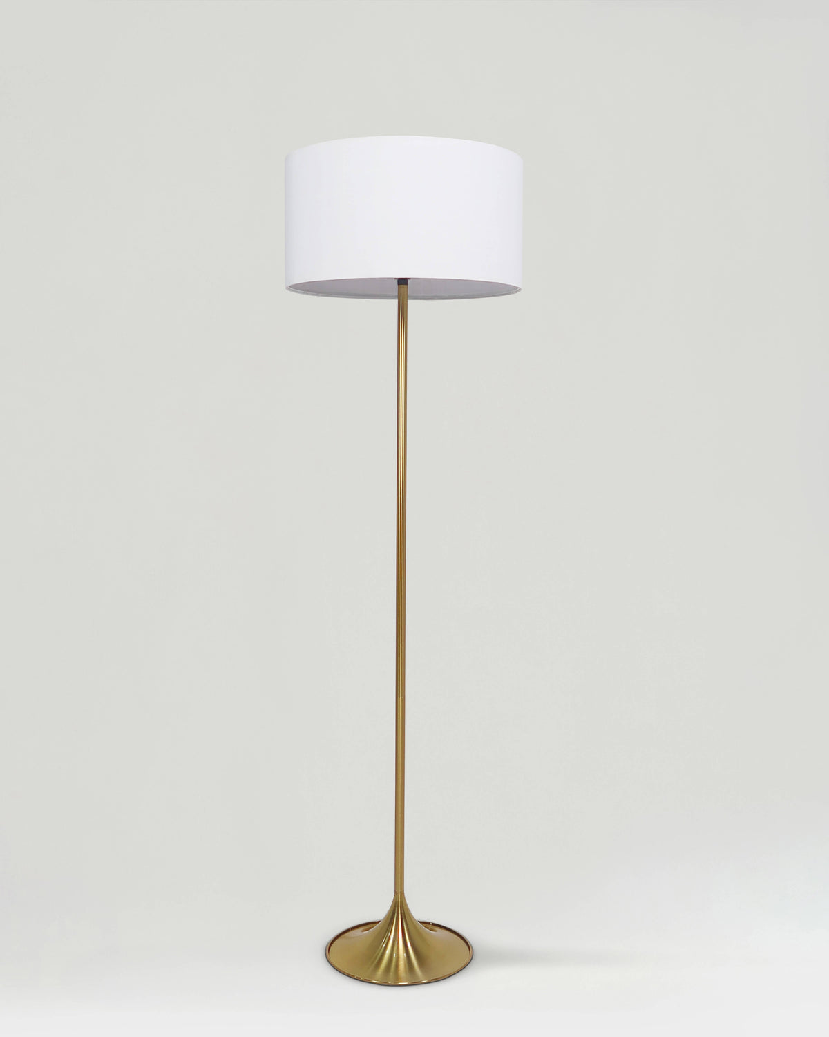 Floor lamp with a white shade and gold base on a light gray background