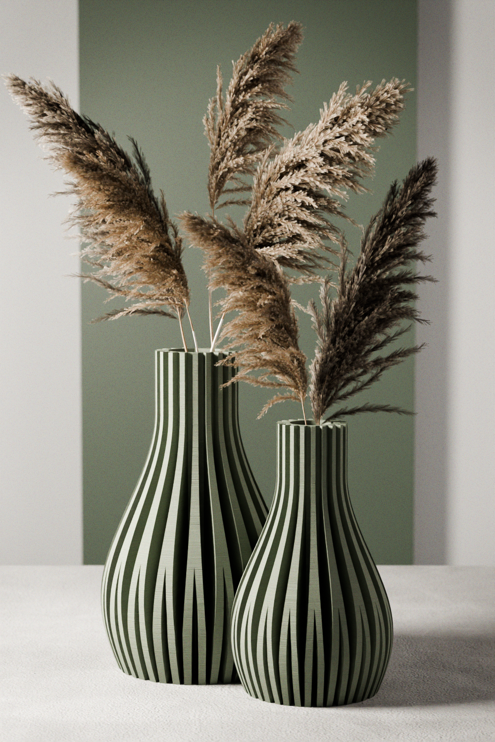 Two ribbed ceramic vases in dark green and beige, filled with dried pampas grass, set against a muted green and white background.